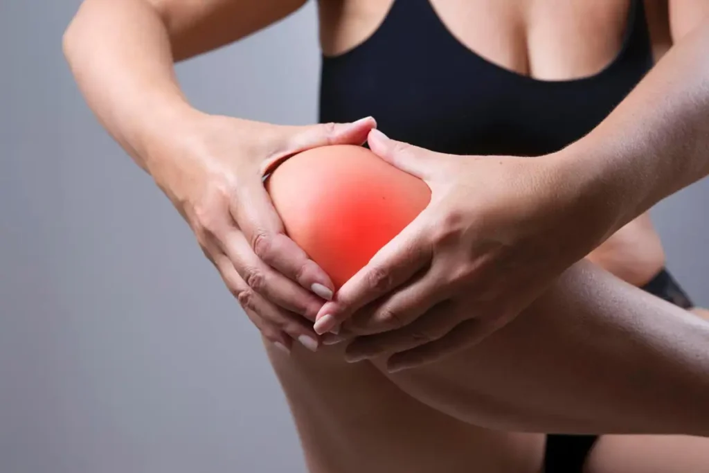 Person fasst sich das rechte Knie nach dem Sport; Fokus auf schmerzenden Bereich.
