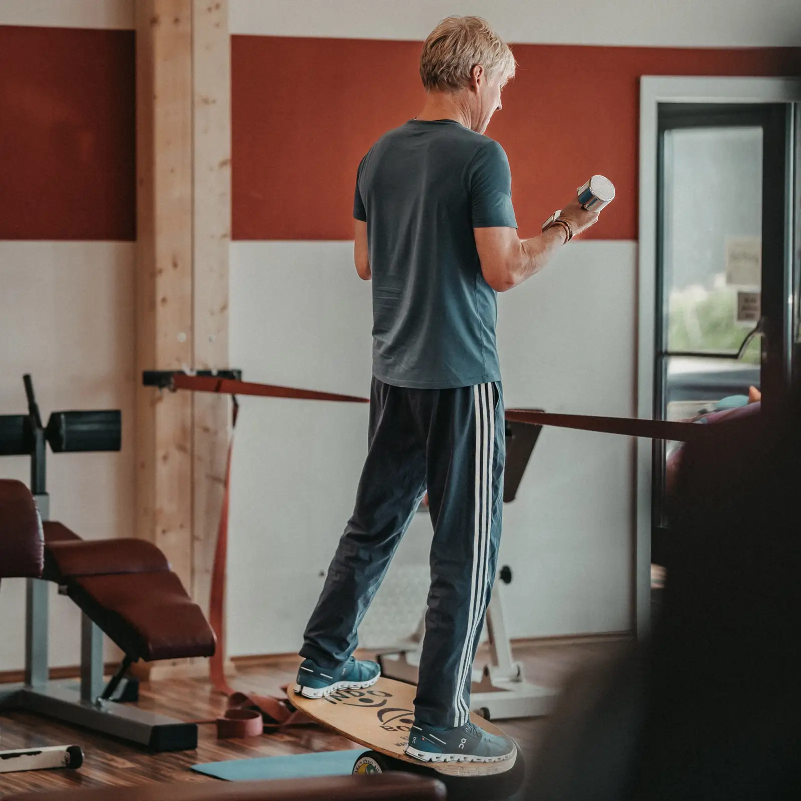 Mann trainiert im Studio auf einem Balance-Board und curlt eine leichte Hantel – Gleichgewicht & Kraft.