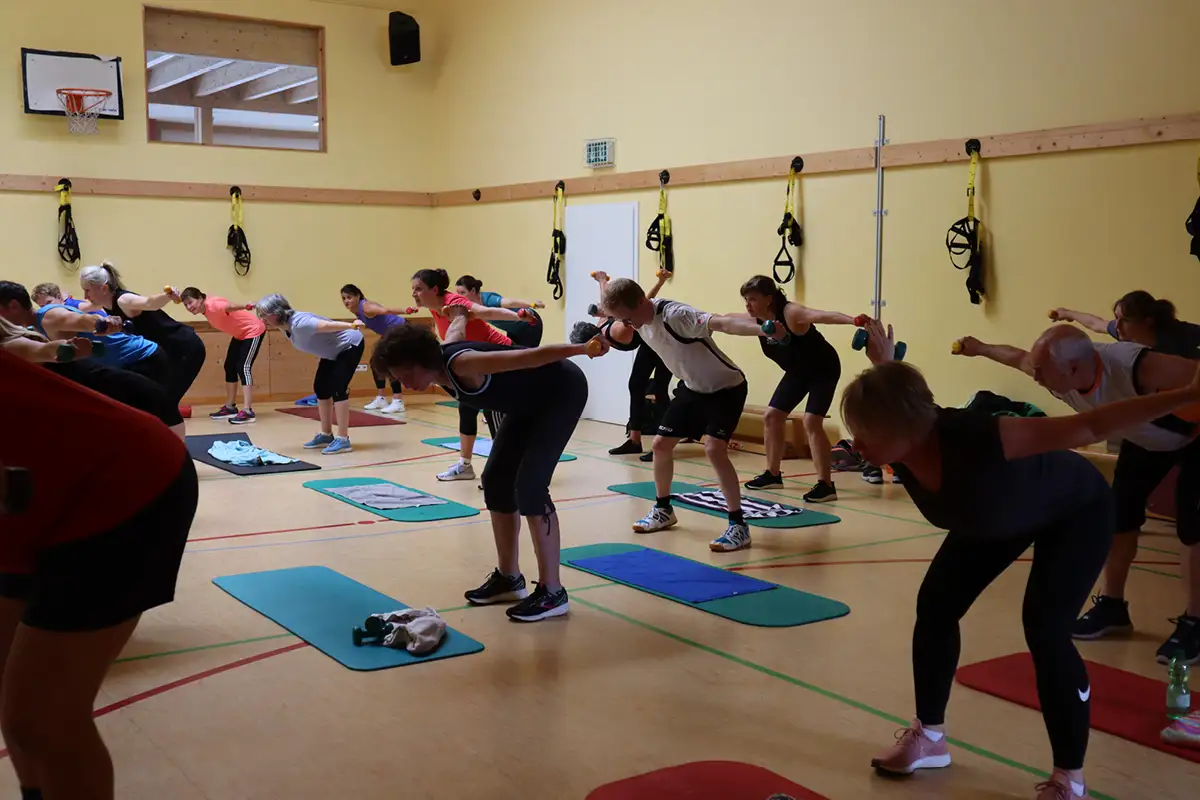 Rehasport-Gruppe übt im hellen Studio mit Trainer*in auf Matten.
