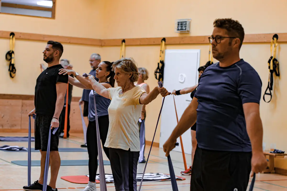 Rehasportkurs im hellen Studio: Teilnehmende üben auf Matten unter Anleitung einer Trainerin.
