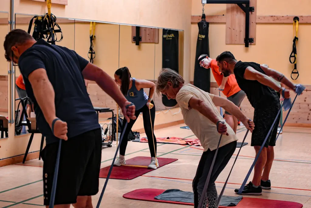 Rehasportkurs im hellen Studio: Teilnehmende üben auf Matten unter Anleitung einer Trainerin.