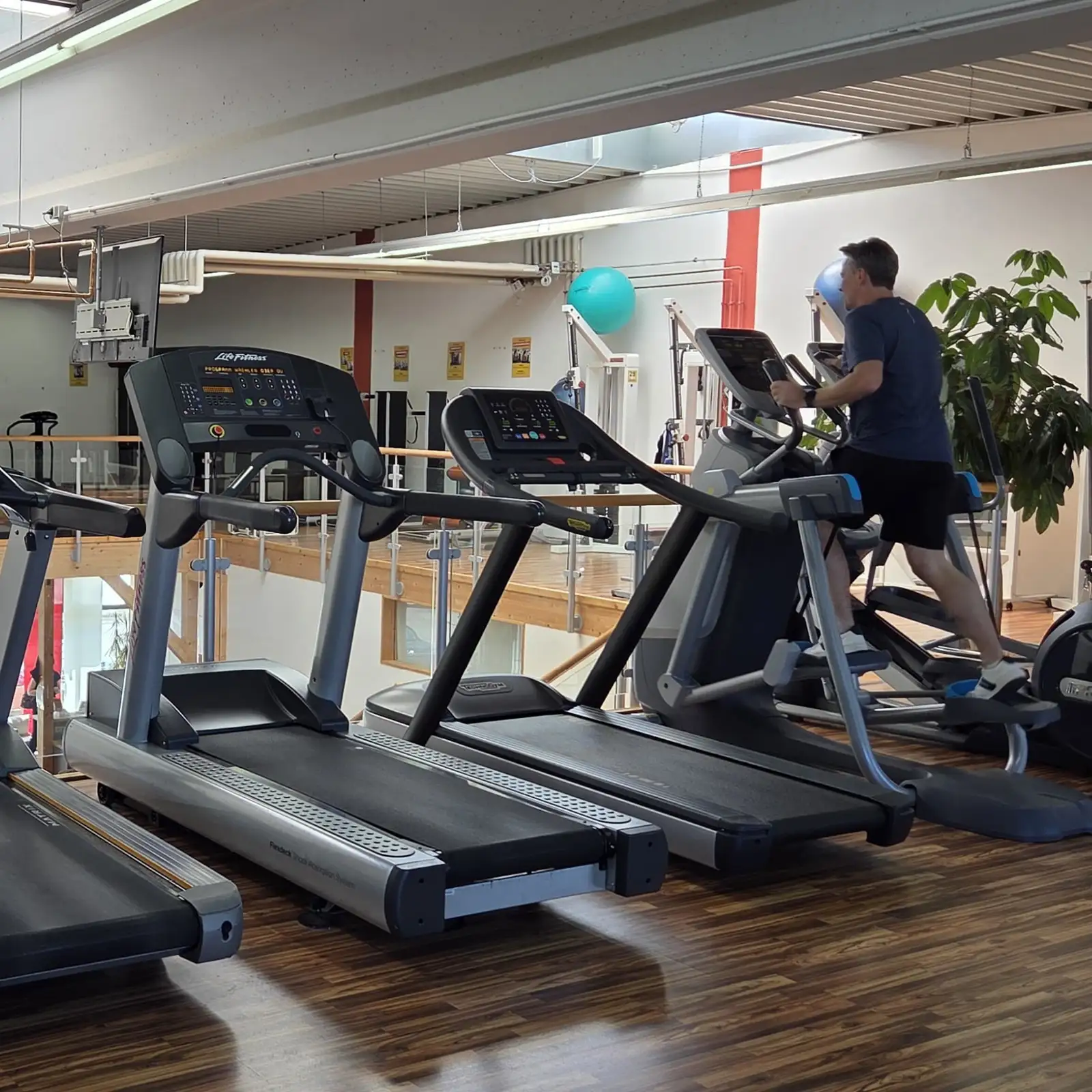 Cardio-Bereich mit mehreren Laufbändern; Person trainiert auf dem Crosstrainer im hellen Studio.